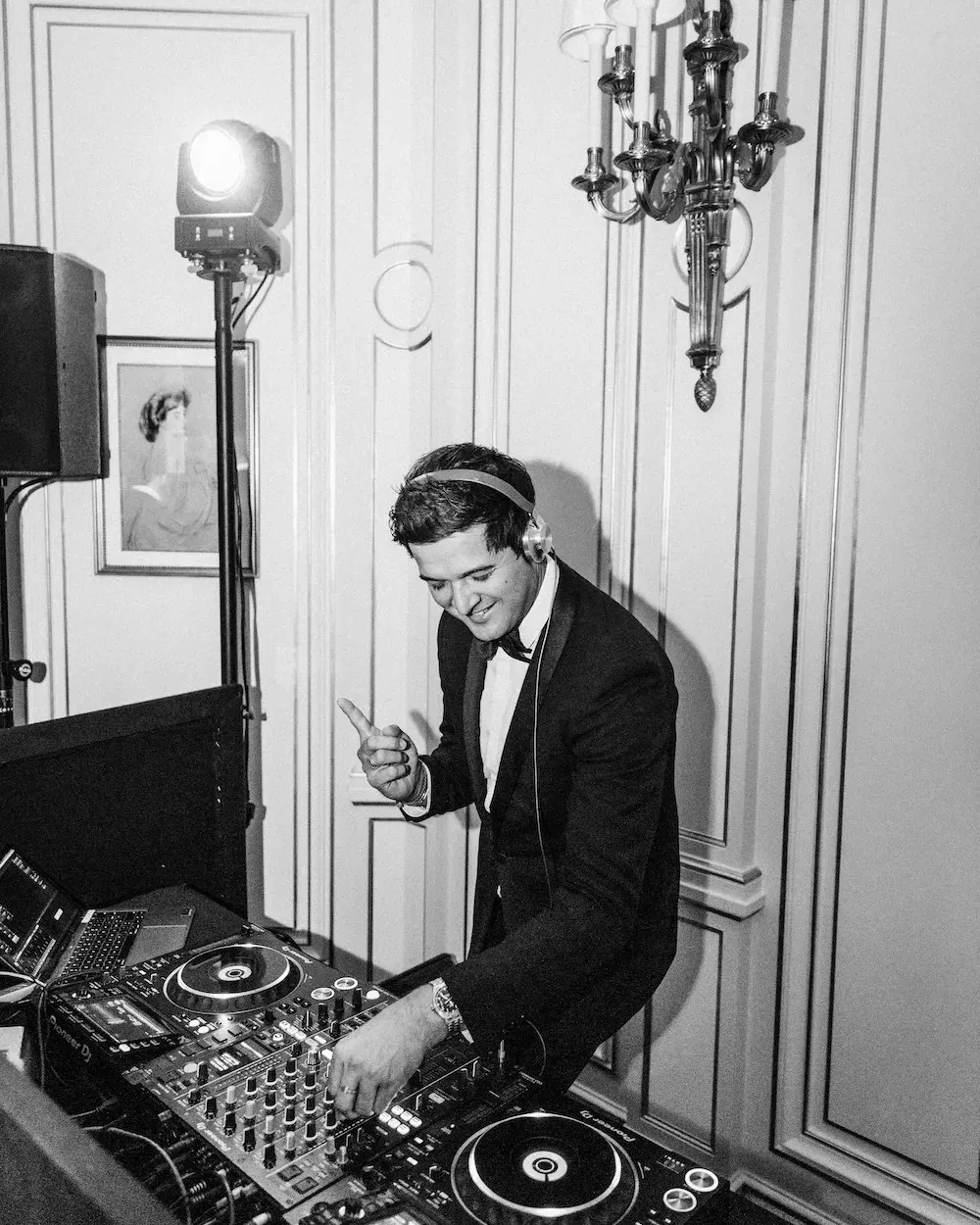 DJ de esmoquin con cascos mezclando junto a un foco y un altavoz