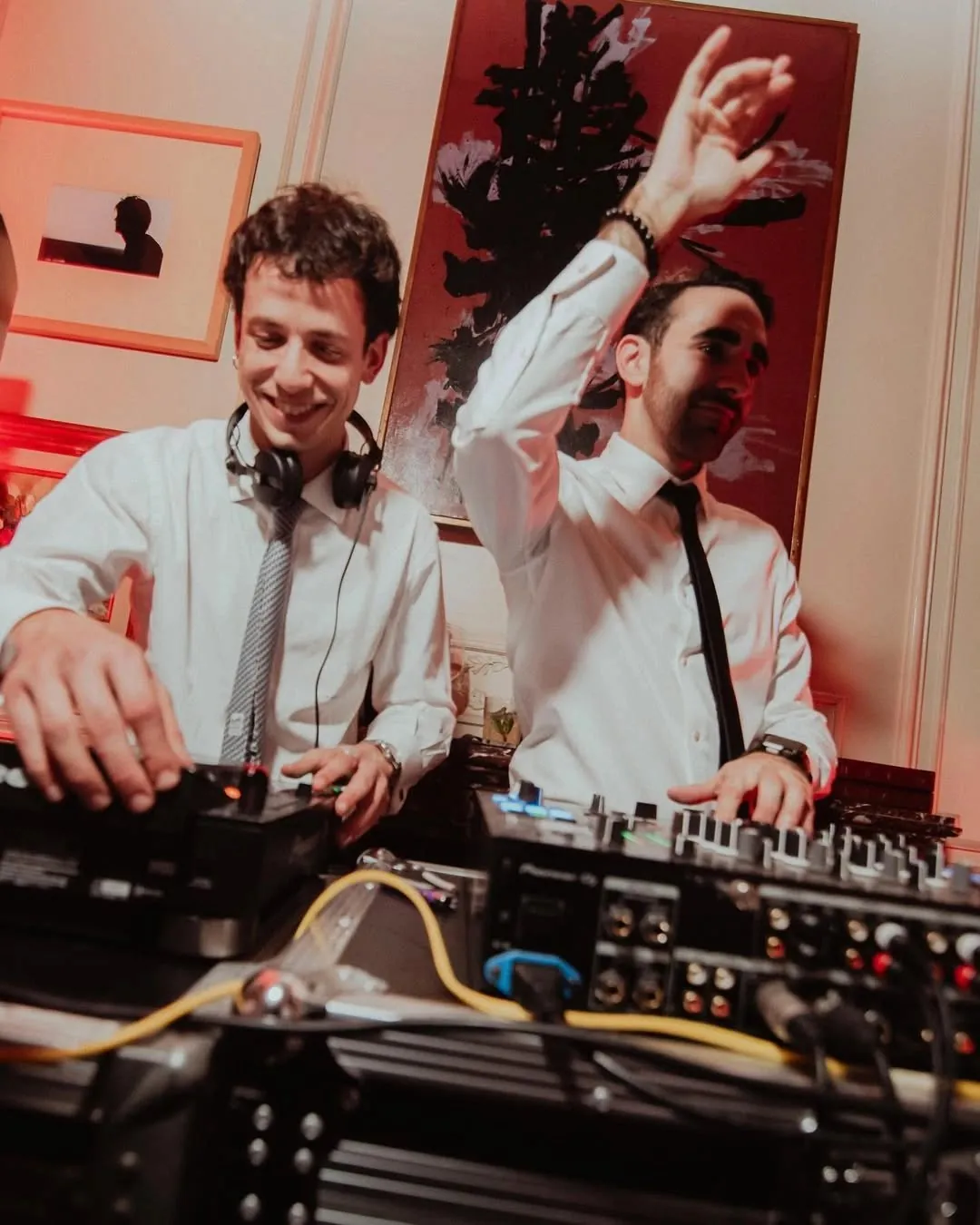 Dos DJs con camisa blanca sonriendo detrás de la mesa de mezclas